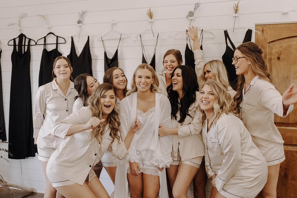 Bridal part getting ready in white silk robes with black dresses in background 