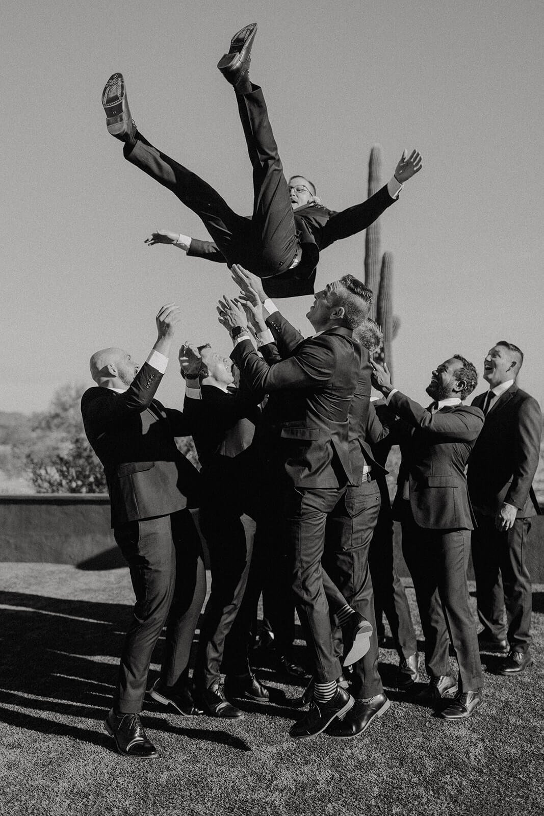 Black and white photo of groomsmen tossing groom in the air