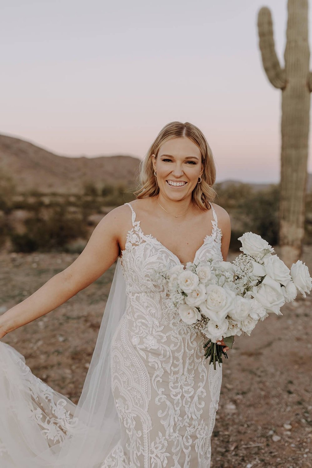 Bride holding bouquet of white roses in the desert with cactus in the background