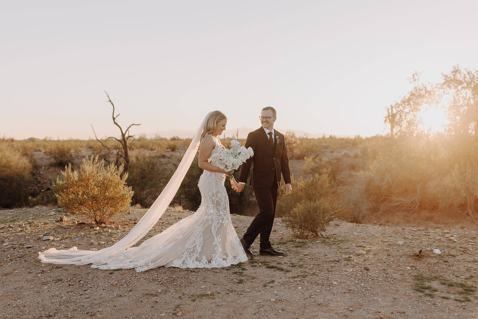 Bride and groom walk through desert at sunset for Arizona destination wedding