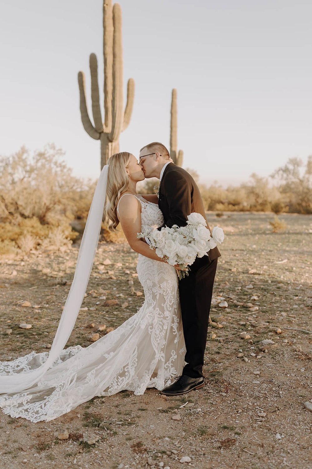 Bride and groom kiss in front of a cactus in the desert in Arizona destination wedding