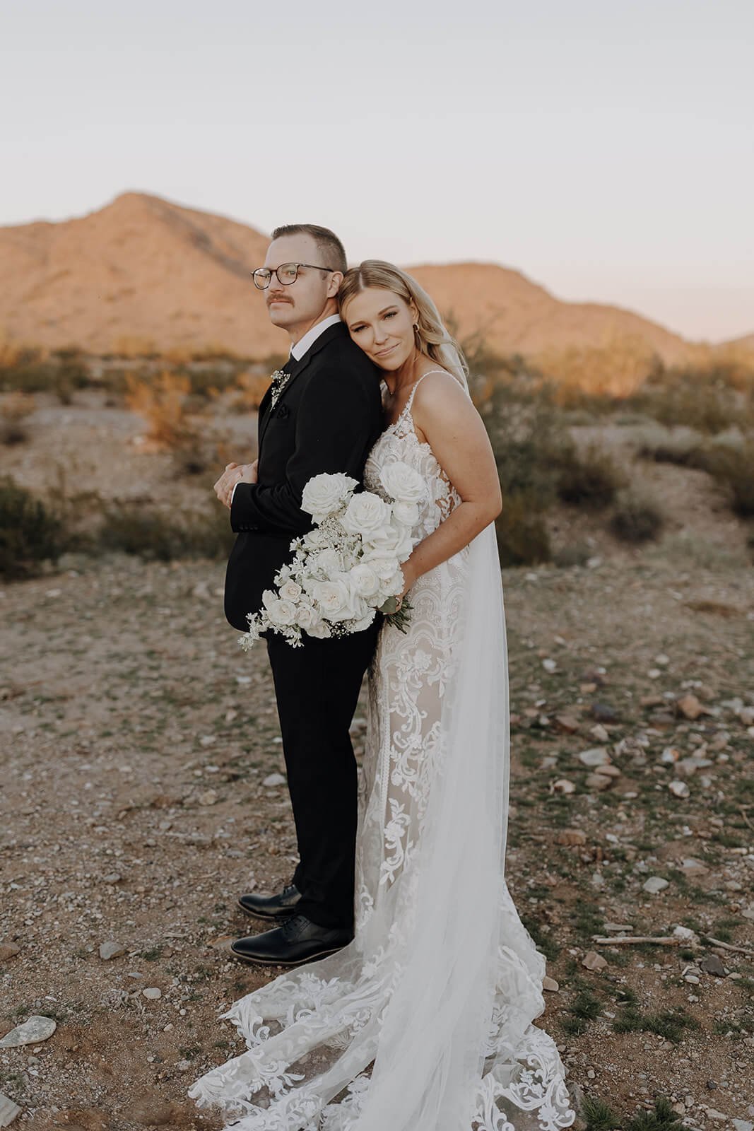 Bride and groom pose in the desert with mountains in the background