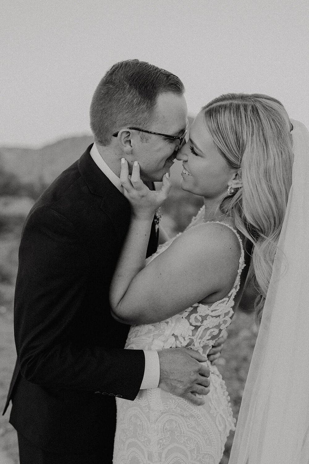 Black and white photo of bride and groom kissing in the desert with mountains in the background