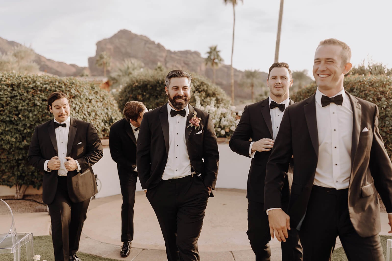 Groom and groomsmen in black tuxedos outside with mountains in background