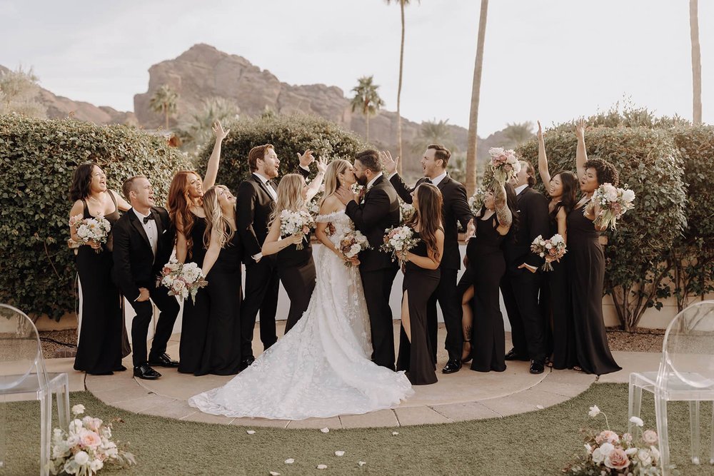 Bride and groom kissing with bridal party around them outside at Scottsdale wedding