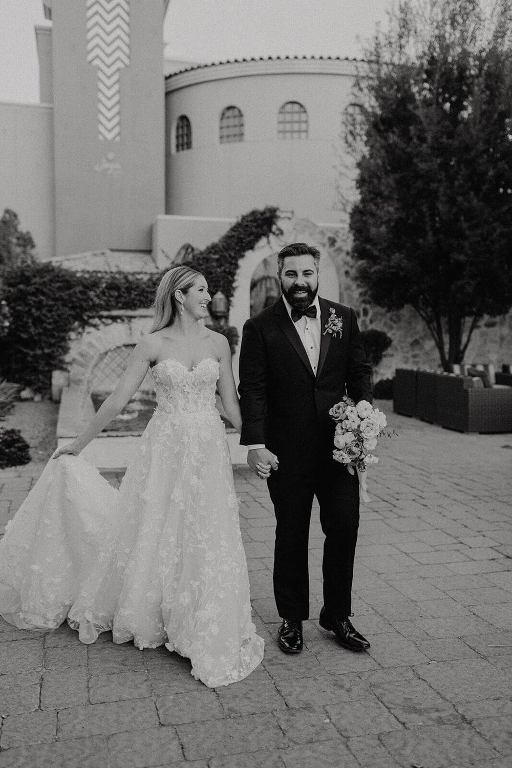 Black and white photo of bride and groom walking outside Spanish style resort