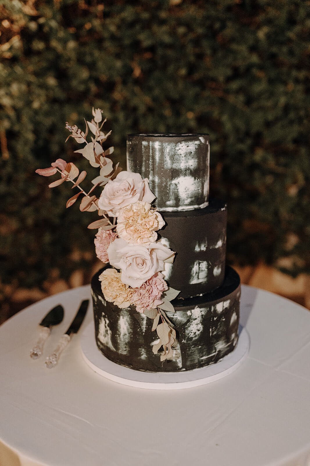 Three-tiered black wedding cake with blush pink floral arrangement