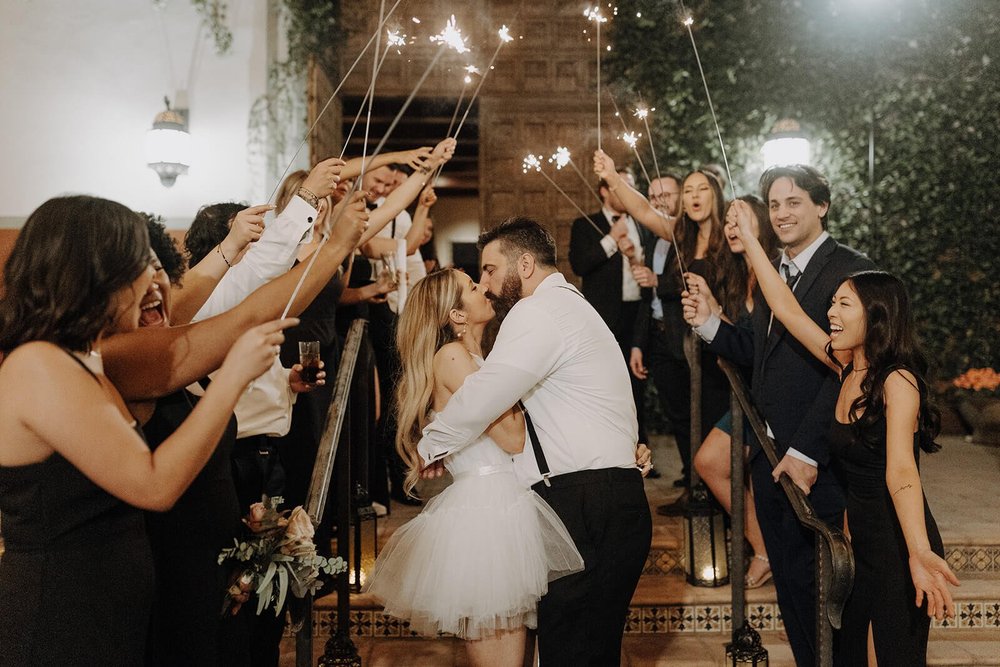 Bride and groom wedding exit, kissing under sparklers with guests