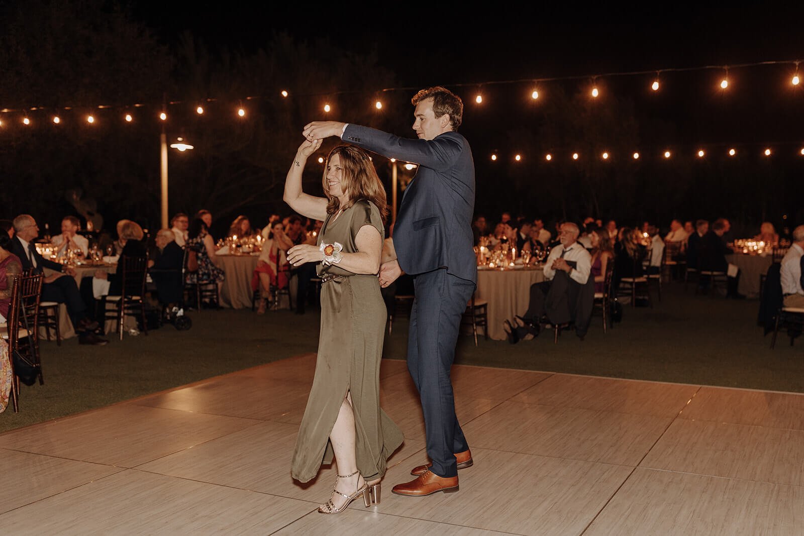 Groom dances with mother at evening outdoor wedding reception