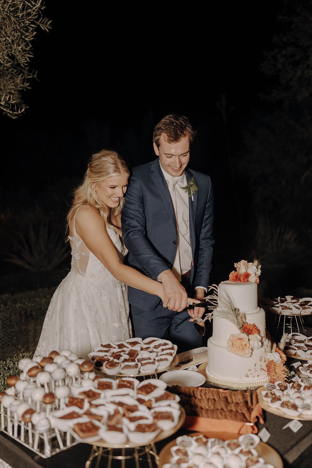 Bride and groom cut cake at outdoor evening wedding reception