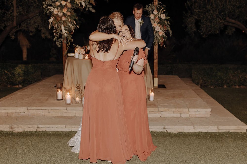 Bride hugs bridesmaids at outdoor evening wedding reception