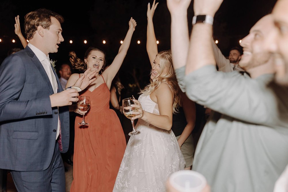 Bride and groom dance with guests at outdoor evening wedding reception