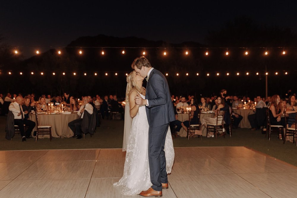 Bride and groom first dance under lights on dance floor at outdoor evening desert wedding reception