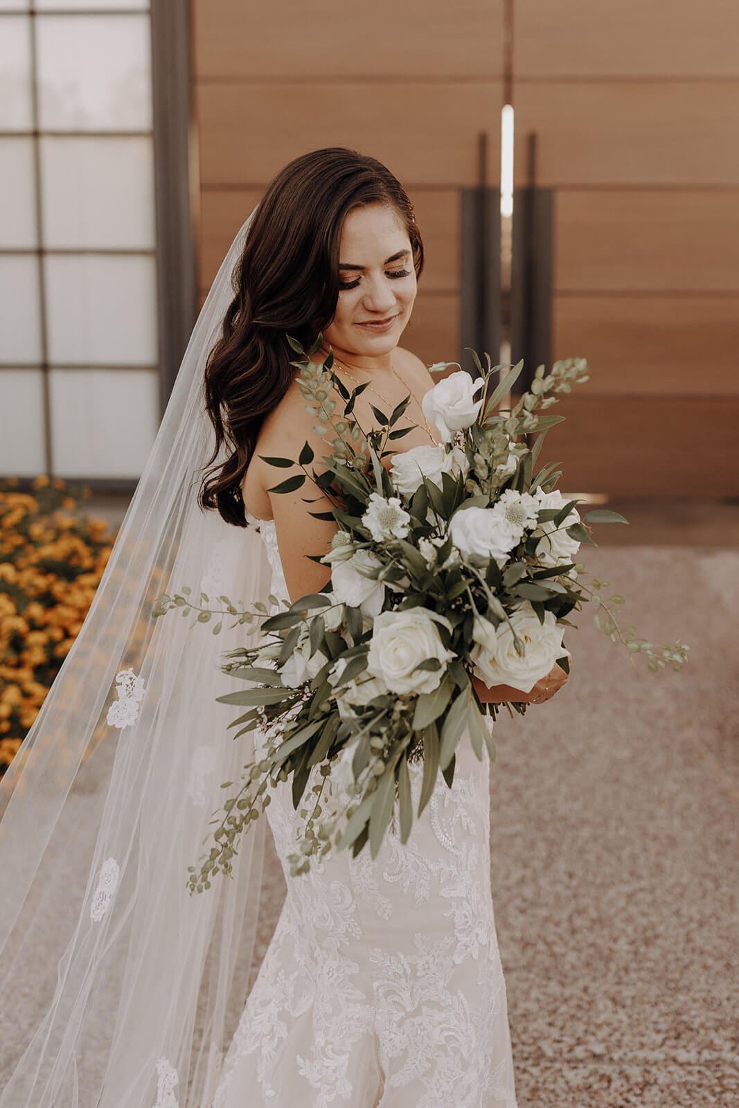 Bride wearing white dress with veil and holding white and green floral bouquet