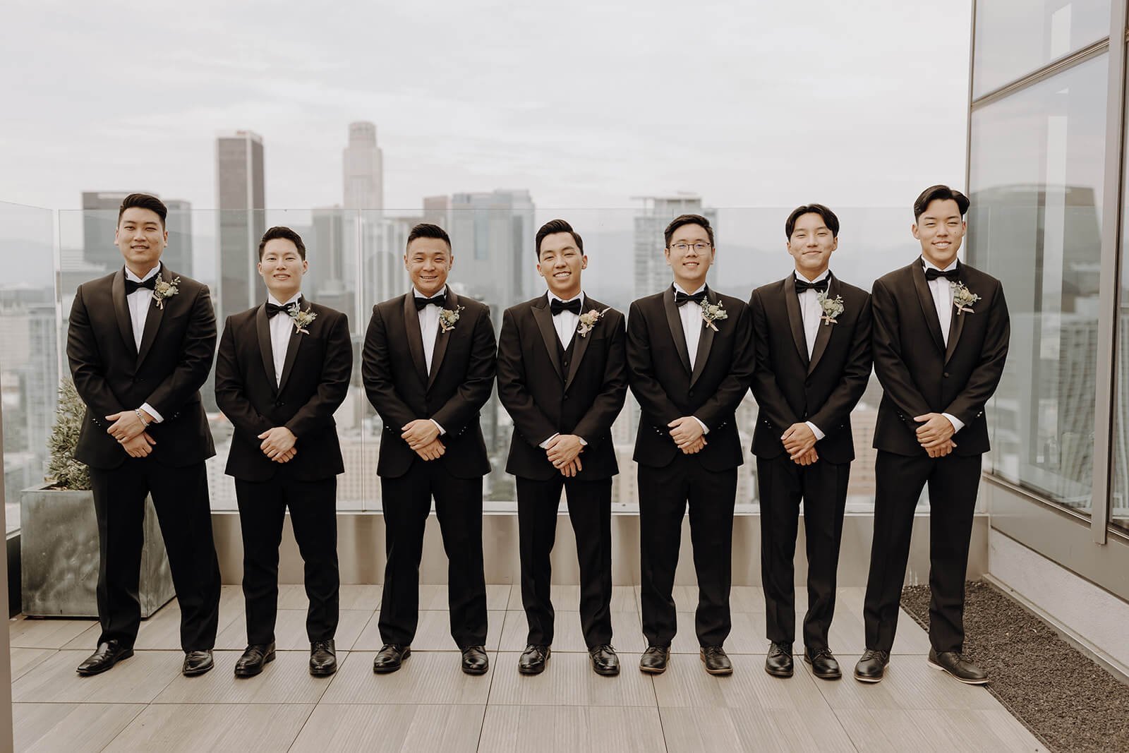 Groomsmen in black tux standing on the top of a building overlooking LA