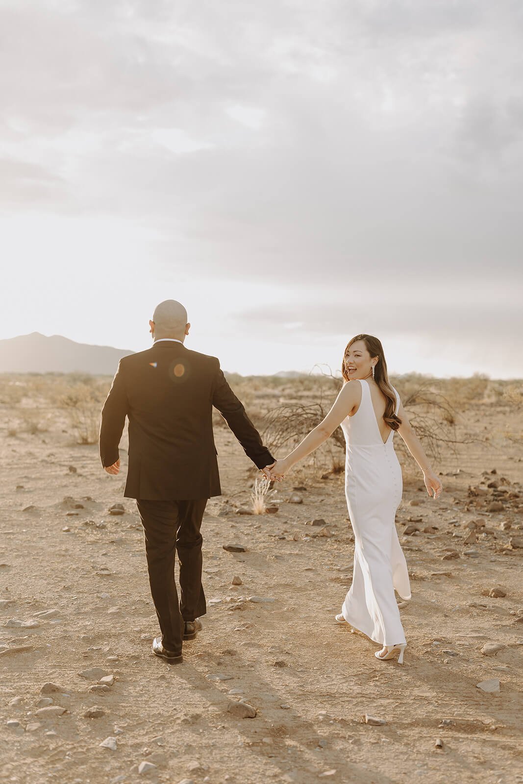 Bride and groom holding hands running through the Arizona desert