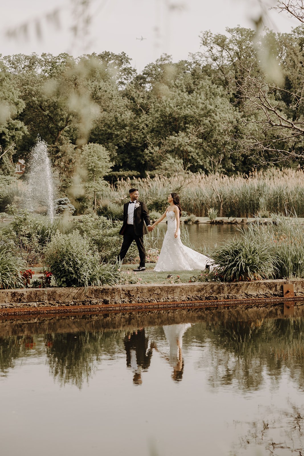 Bride and groom stroll through a garden along a river at luxurious wedding venue in NY