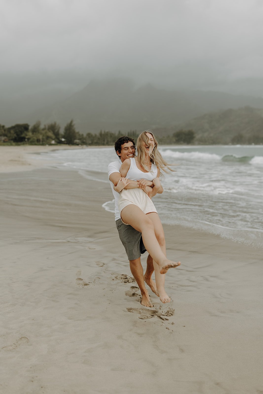 Man swinging woman around on the beach in Kauai for Hawaii engagement photos
