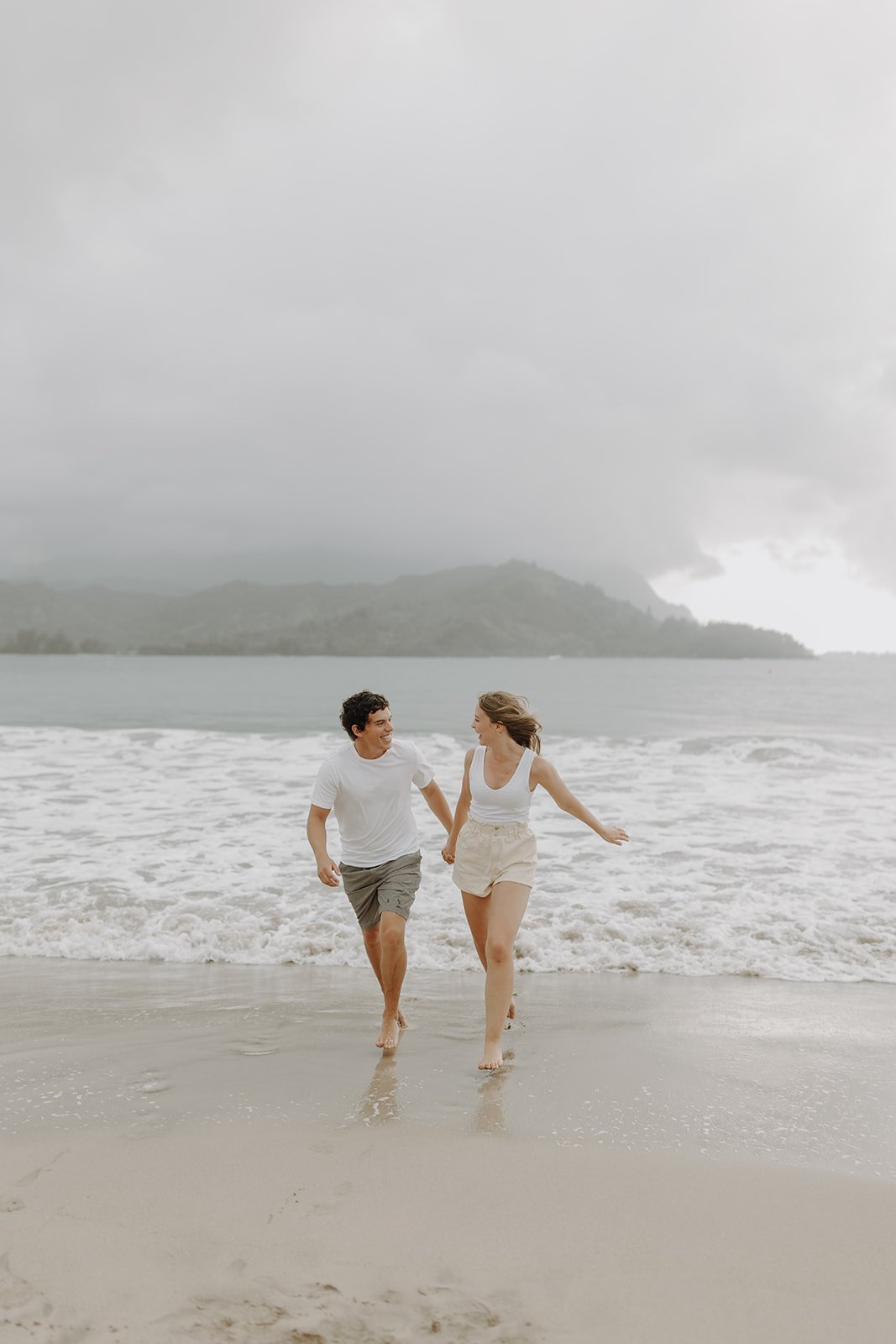 Couple holding hands and running across the beach in Kauai for their Hawaii engagement photos