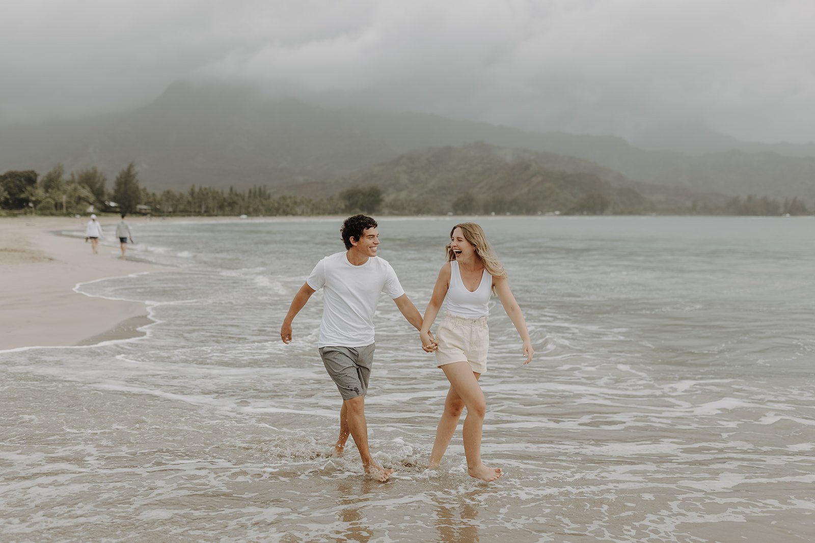 Couple holding hands and running across the beach in Kauai for their Hawaii engagement photos