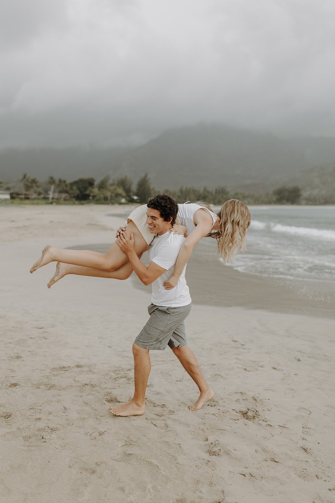 Man carrying woman across the beach for Kauai engagement photos