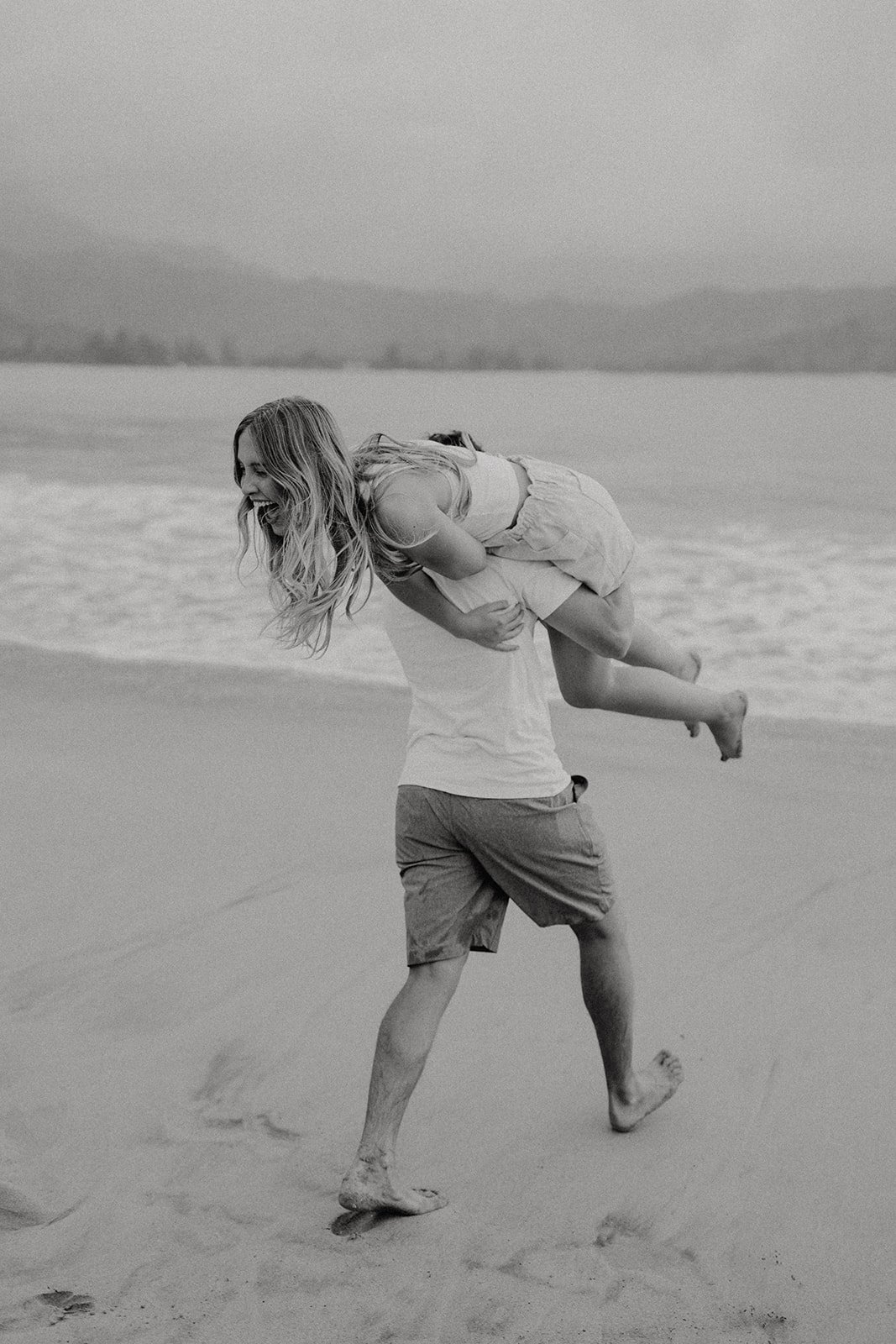 Man carrying woman across the beach for Kauai engagement photos