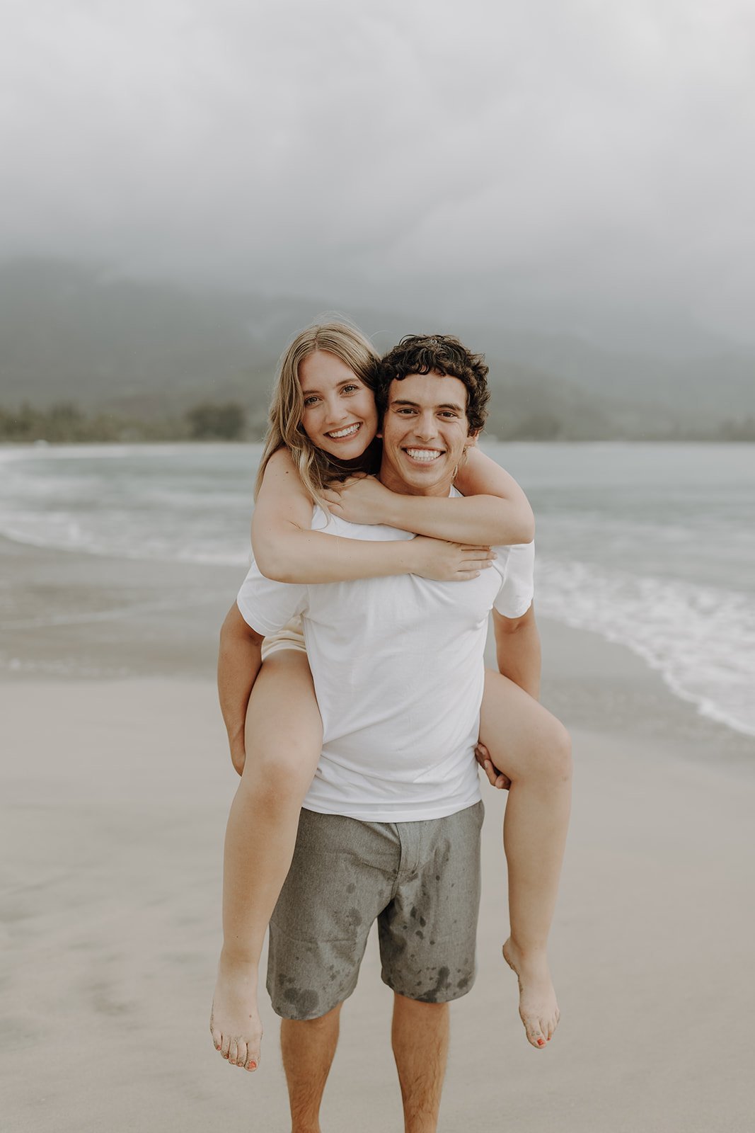 Woman riding on man's back during engagement photo session in Kauai