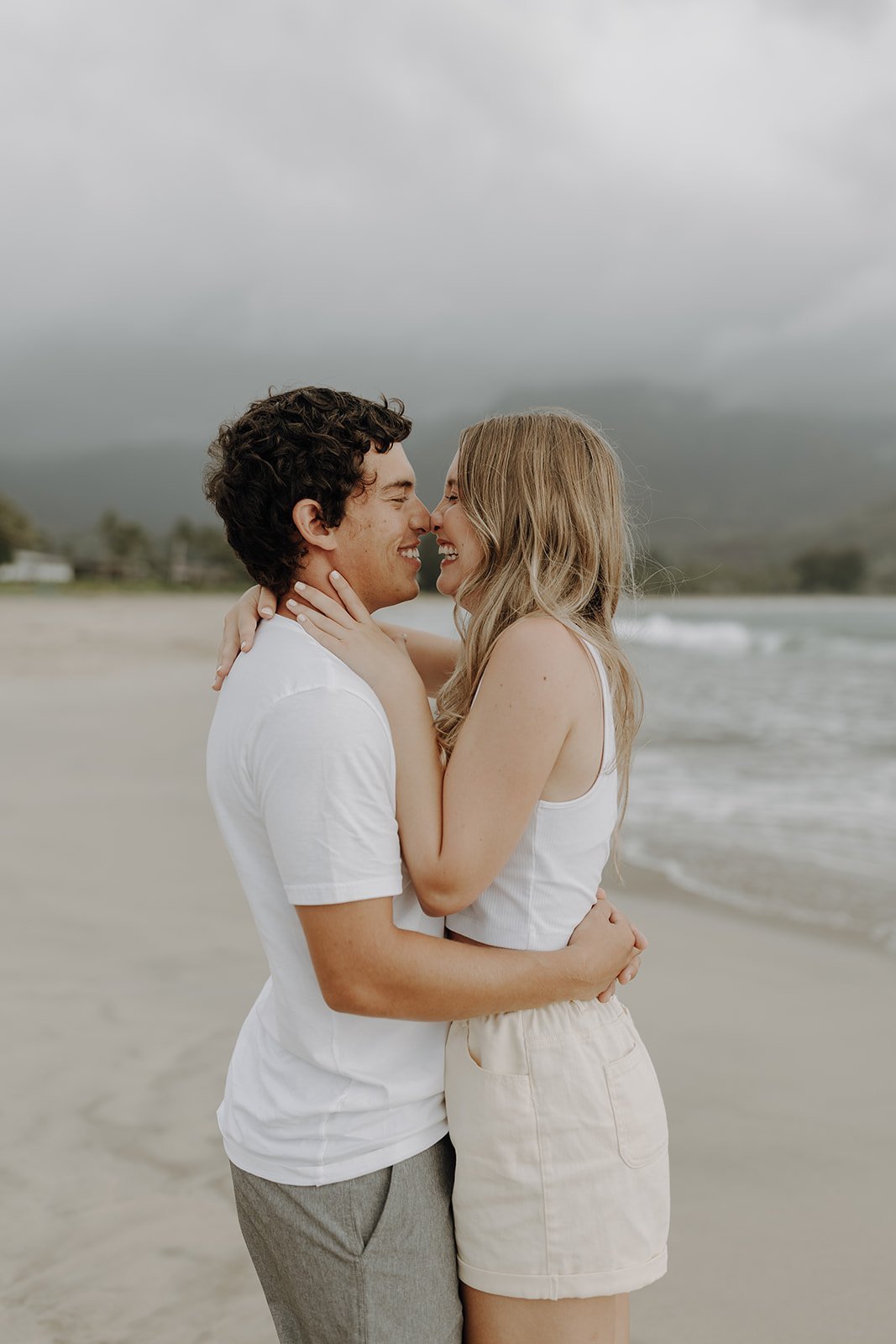 Couple kissing and laughing on the beach during engagement photo session in Hawaii