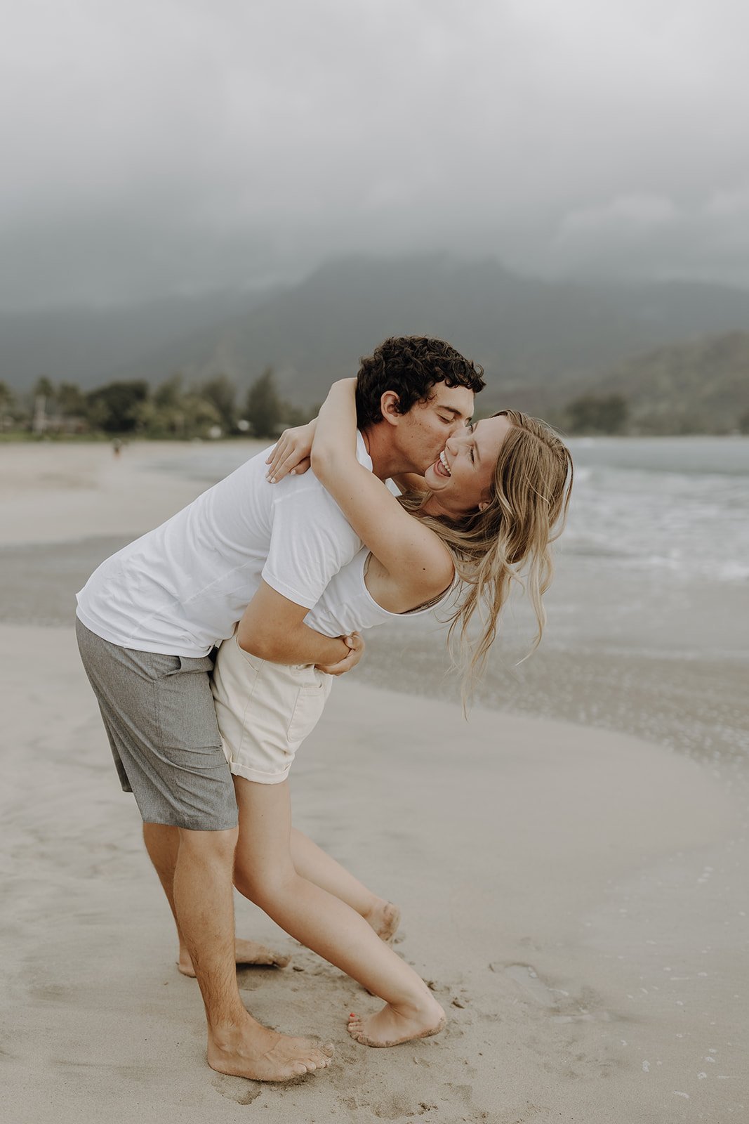 Man kissing woman on the cheek and dipping her backwards during engagement photo session in Hawaii