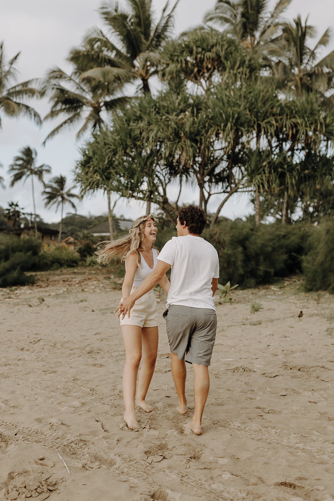Couple holding hands and dancing around on the beach for Kauai engagement photos
