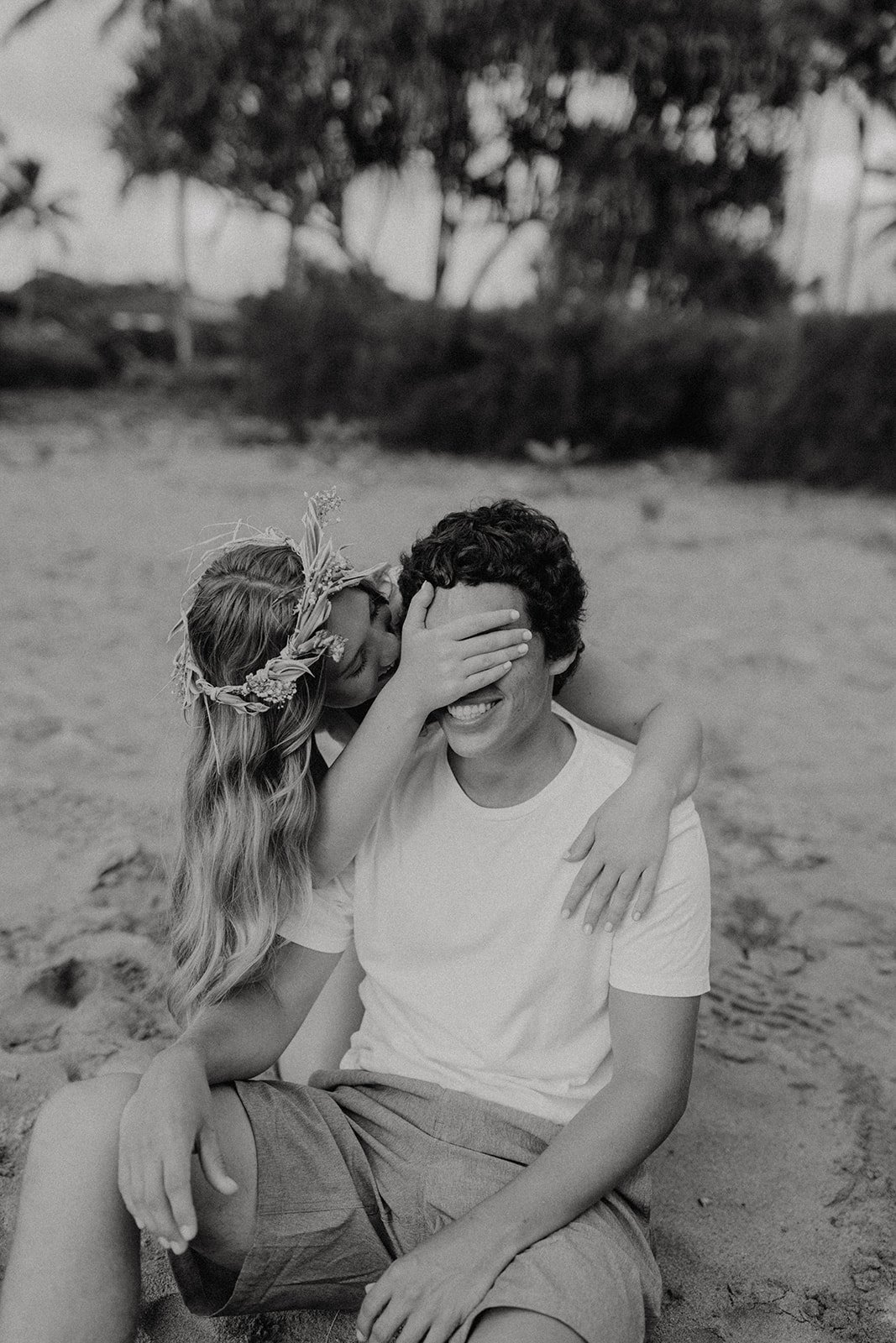 Woman covering man's eyes while sitting on the beach during Hawaii engagement photos