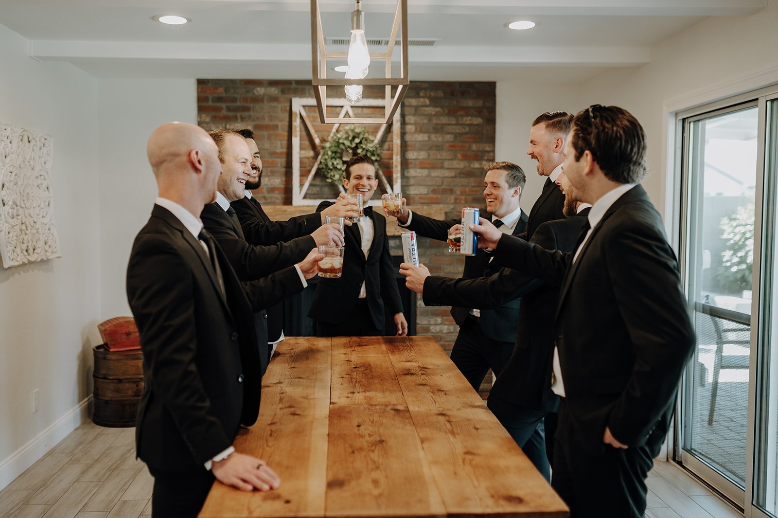 Groom and groomsmen in black suits toasting over a wood table 