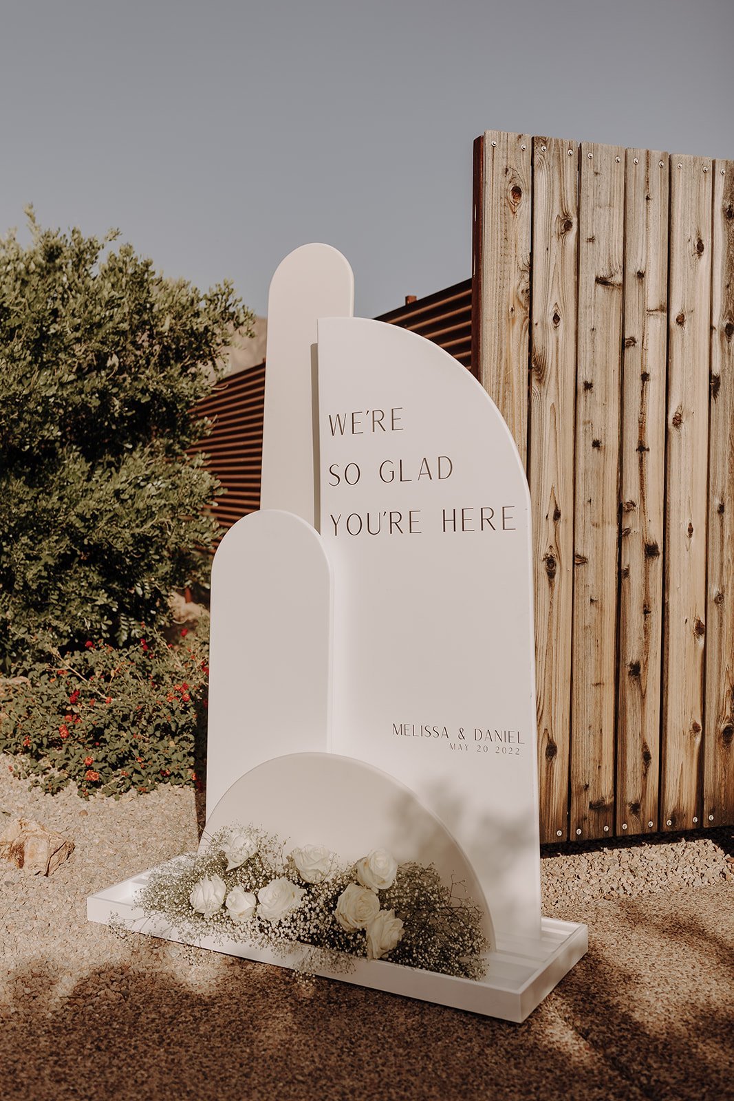 White modern wedding sign that reads "We're So Glad You're Here"