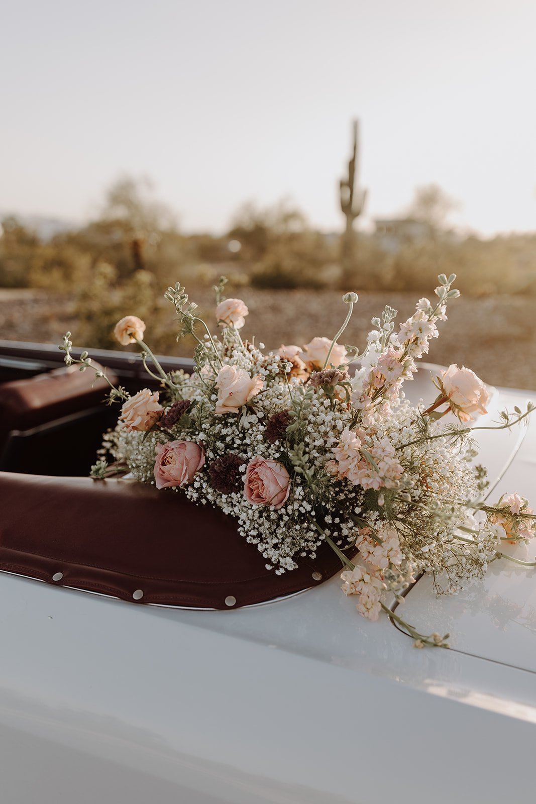 Pink and white flowers sitting on top of a vintage white convertible