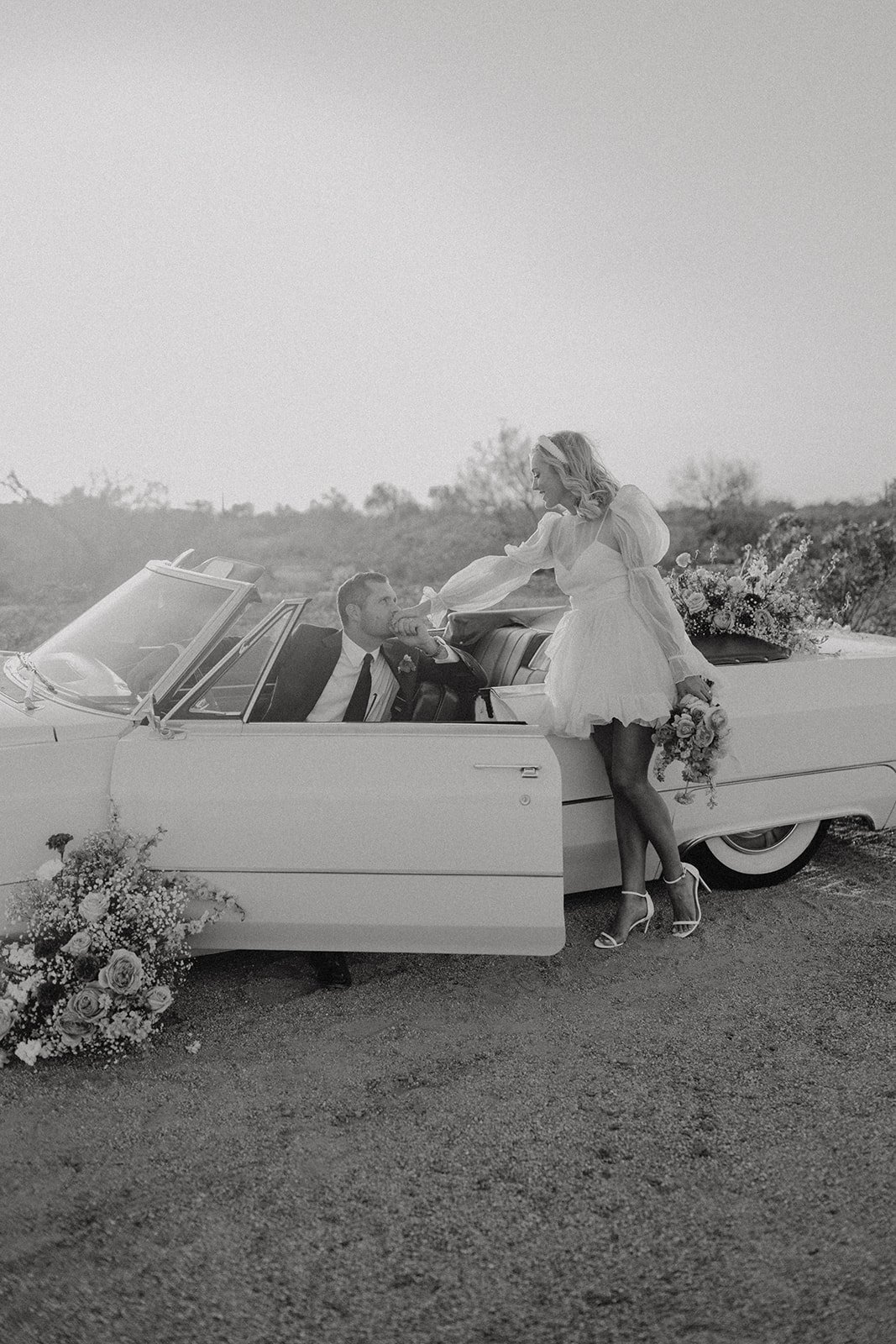 Bride reaching for groom inside vintage white convertible