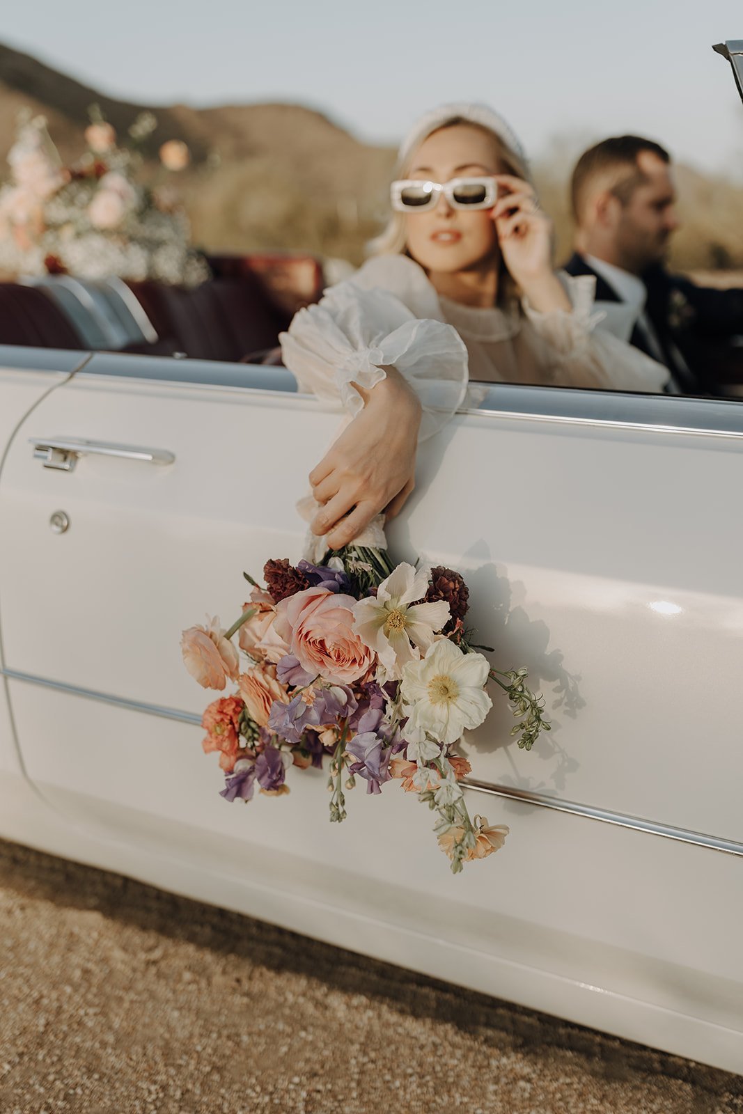 Bride holding white and pink bouquet outside vintage white convertible