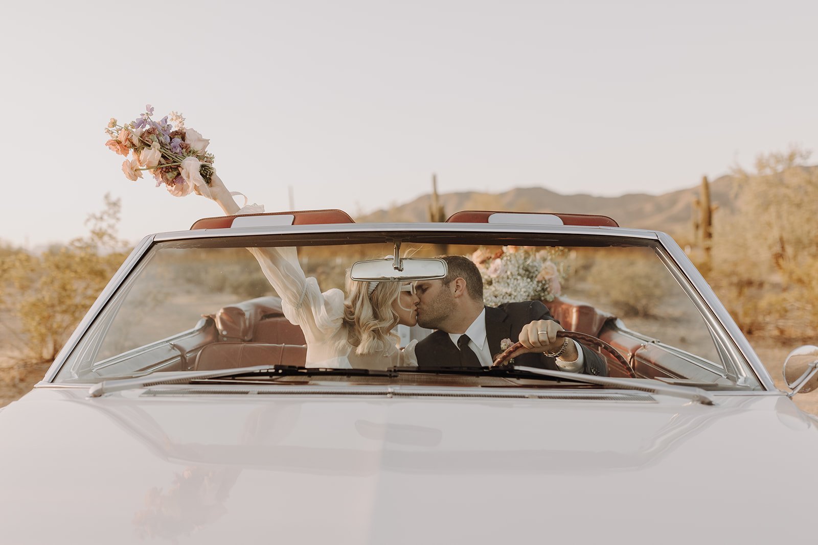 Bride and groom kissing in vintage white convertible