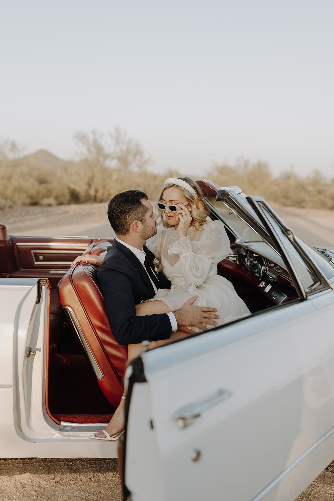 Bride sitting on groom's lap in vintage white convertible