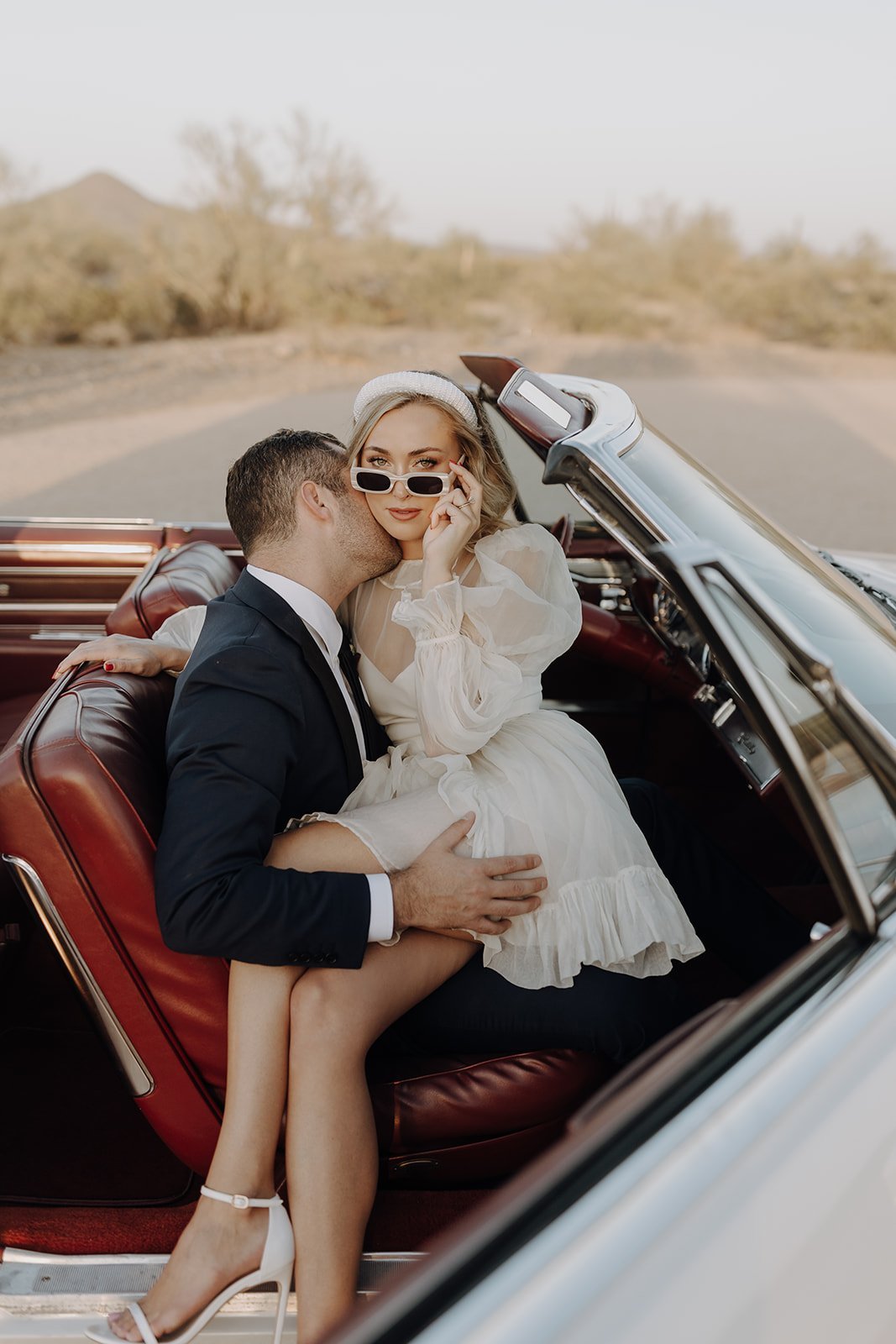 Groom kissing bride's neck in vintage white convertible