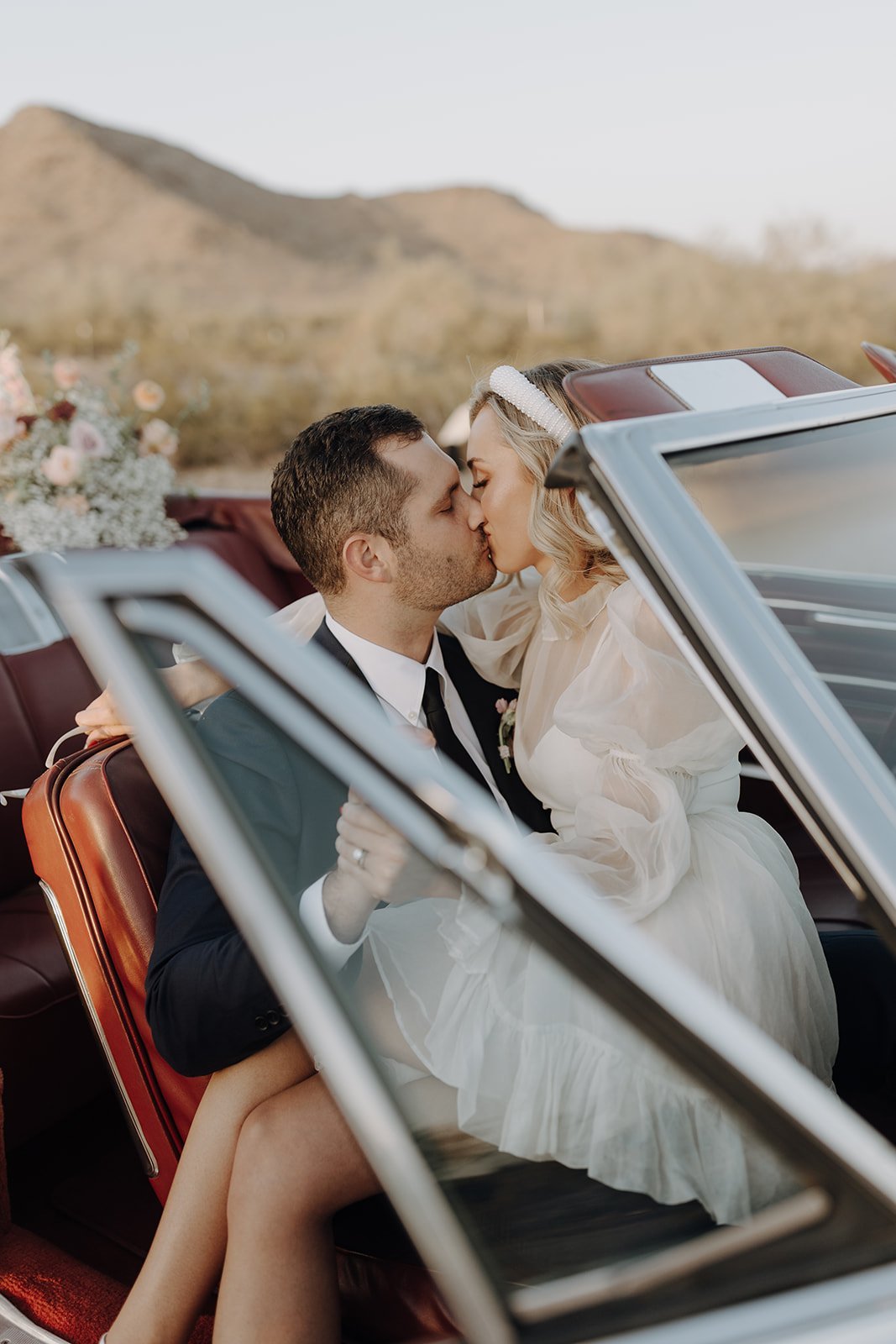 Bride and groom kissing in vintage white convertible