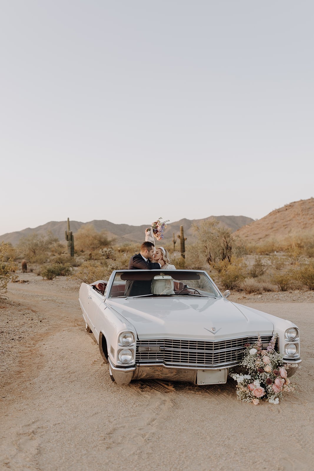 Bride and groom sitting in the backseat of vintage white convertible for wedding styled shoot