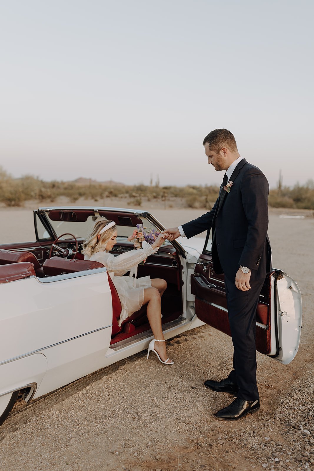Groom helping bride out of vintage white convertible
