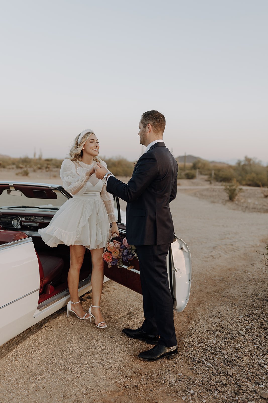 Groom helping bride out of vintage white convertible