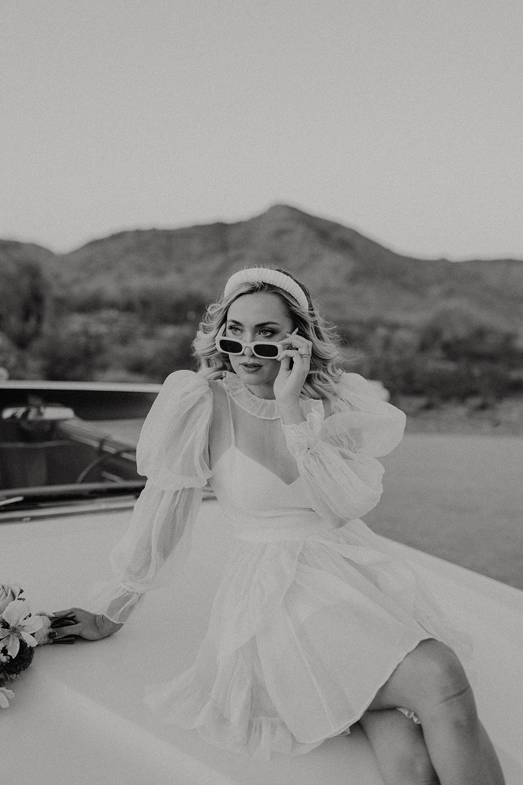 Bride pulling down sunglasses while sitting on top of vintage white convertible