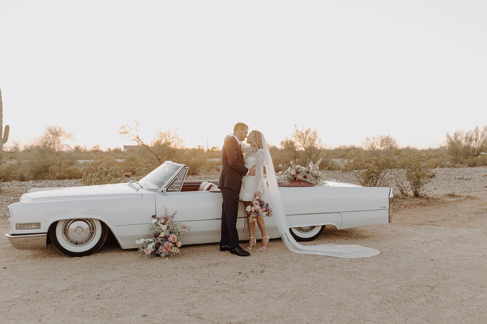Bride and groom standing beside a vintage white convertible for wedding styled shoot