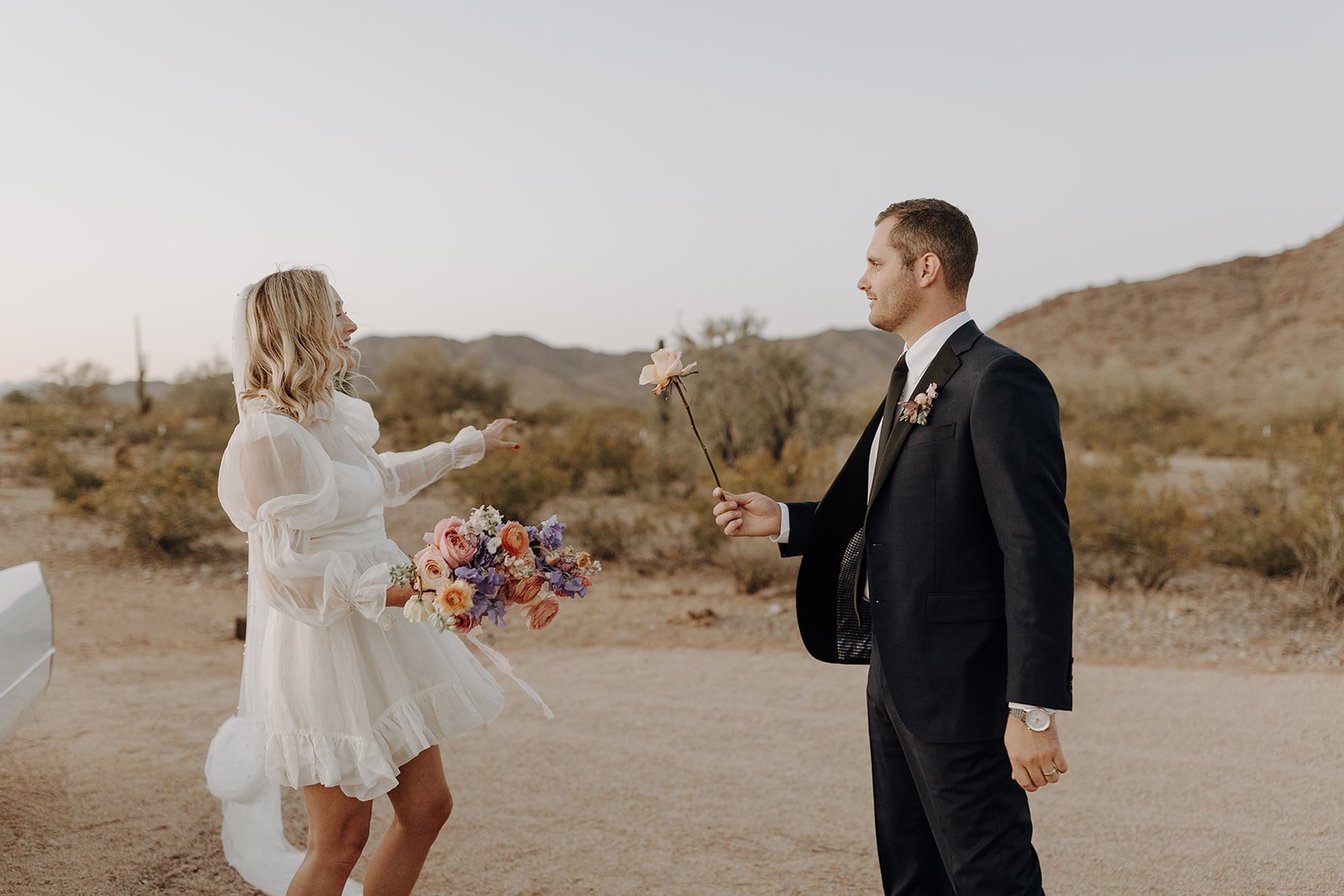Groom handing bride a pink rose during wedding styled shoot