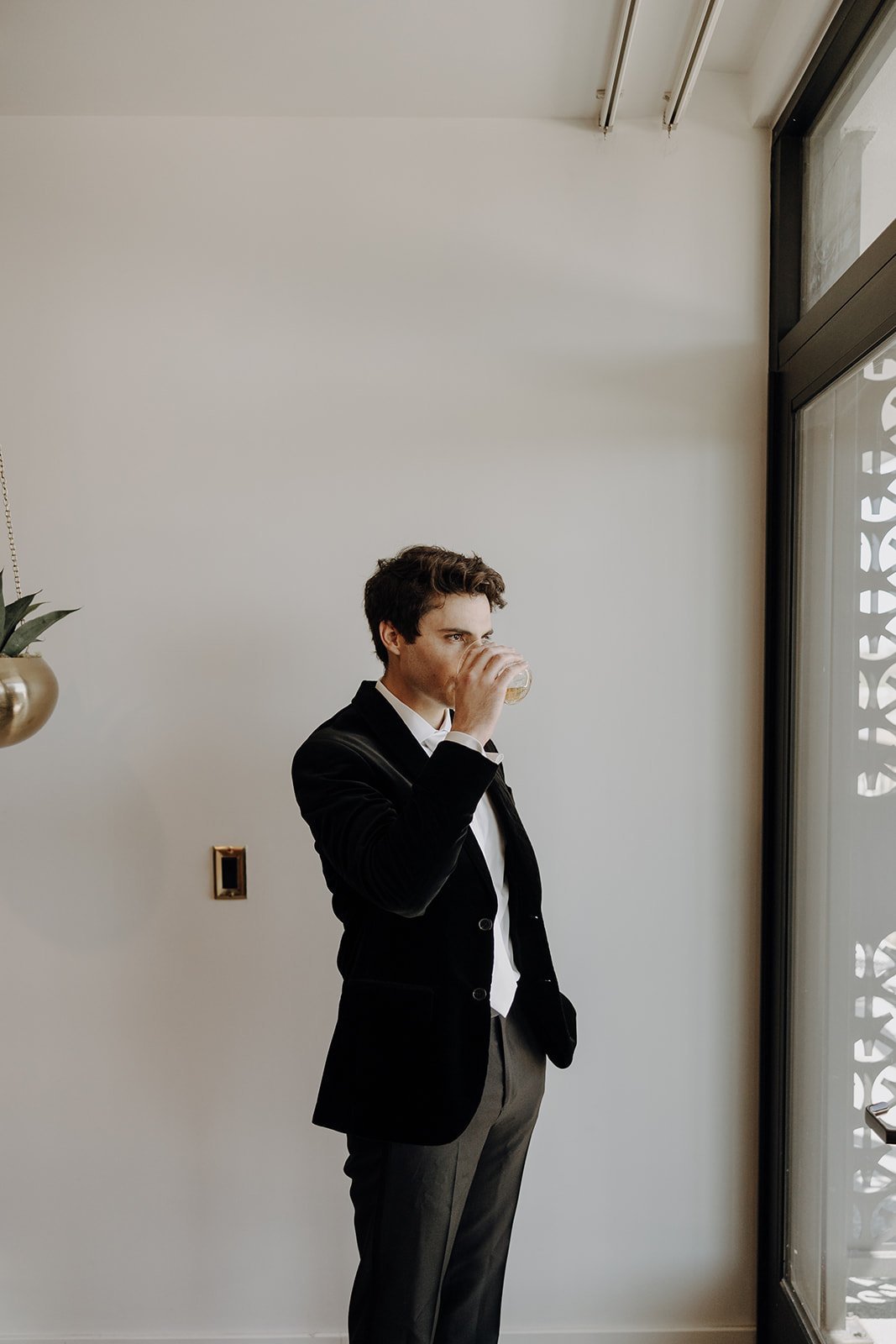 Groom in a black suit sipping alcohol on wedding morning