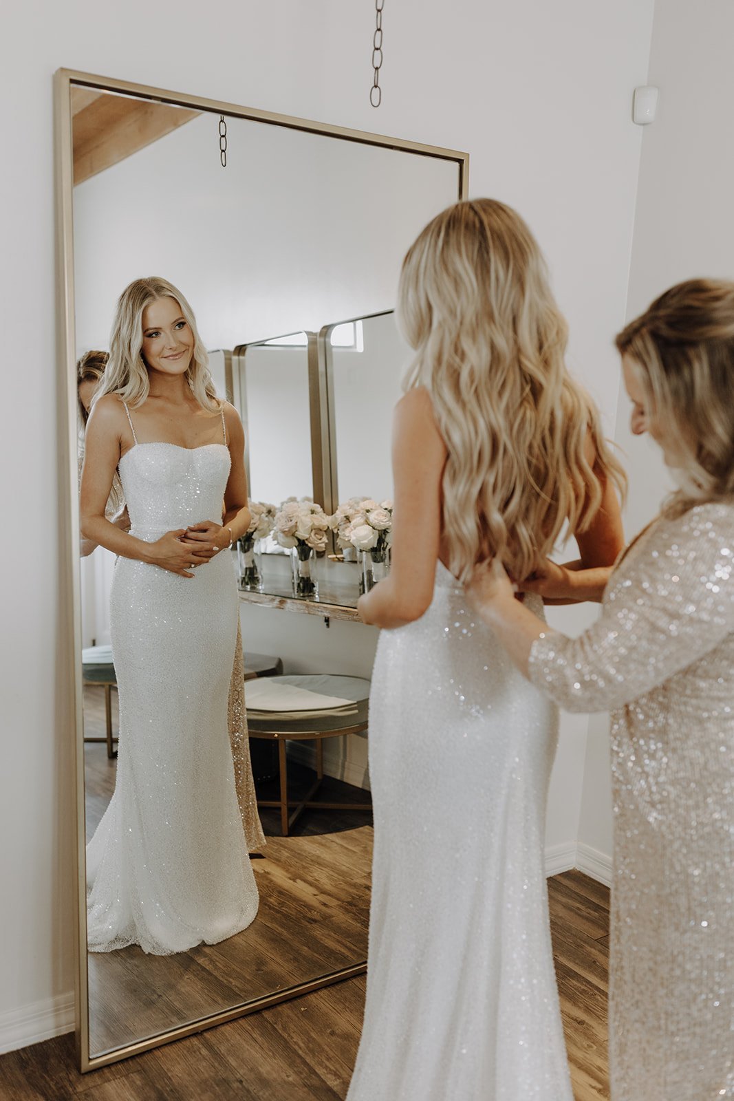 Bride smiling in the mirror while her mother zips her wedding dress