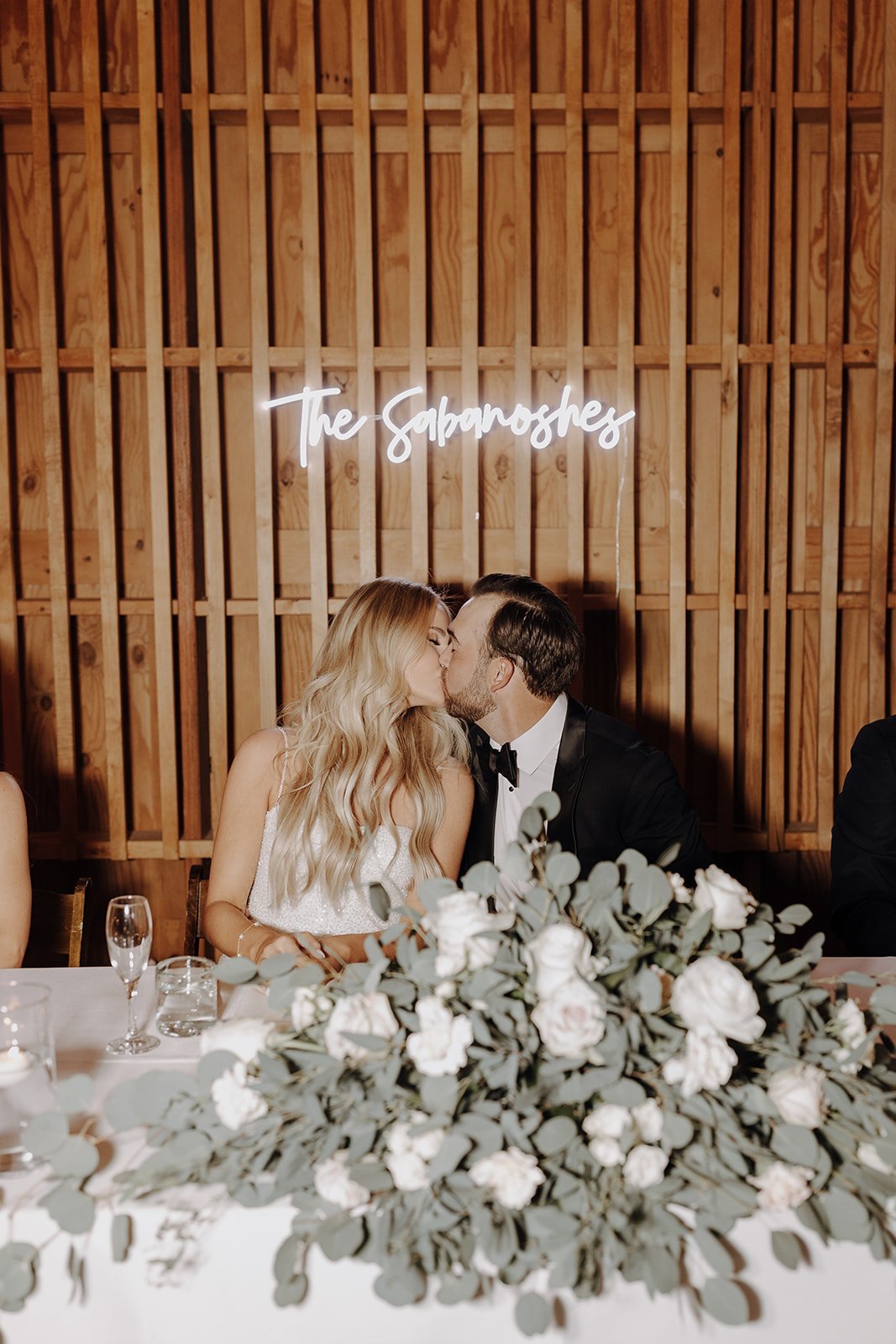 Bride and groom kiss at their reception tabled with neon sign in the background