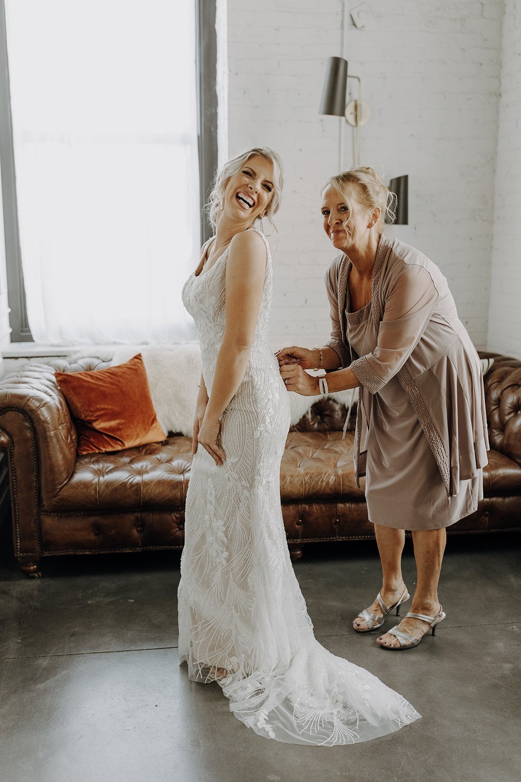 Bride and mother zipping up wedding dress while getting ready